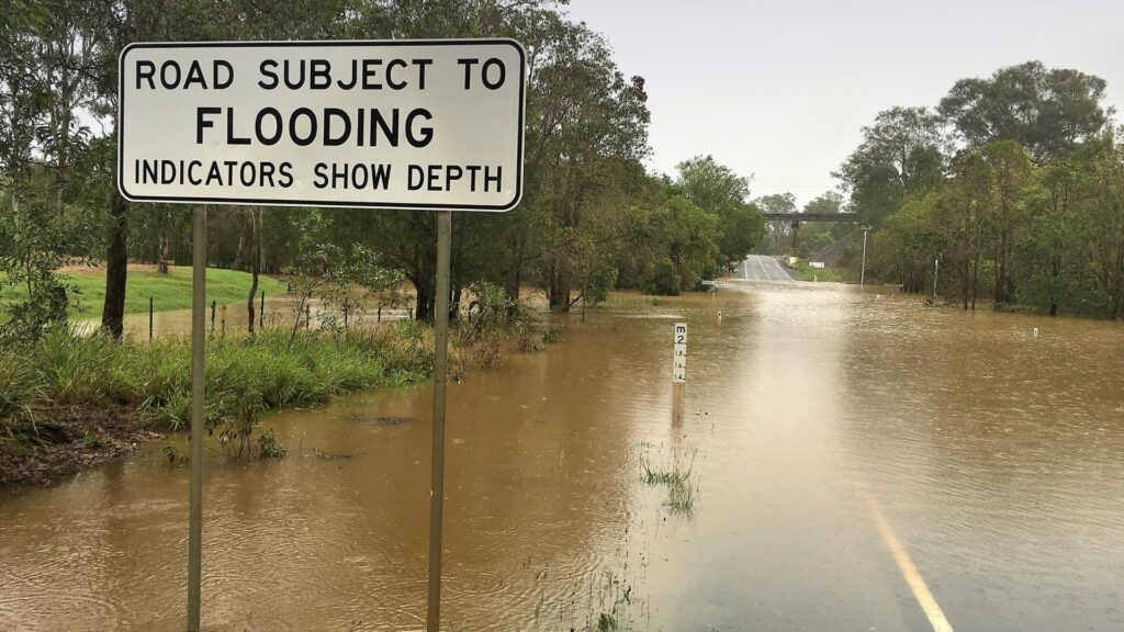 A flood warning sign in a flooded roadway.